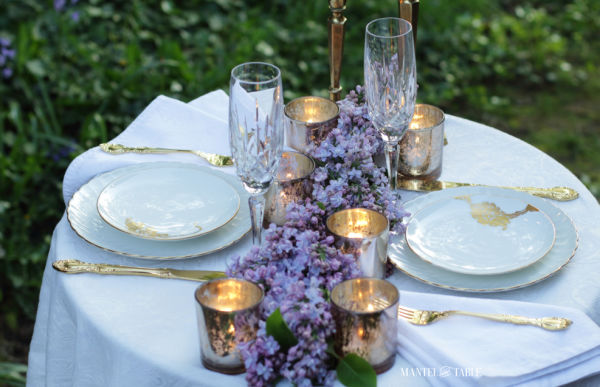 lilac garland on white linen decorates an outdoor candlelight dinner for two