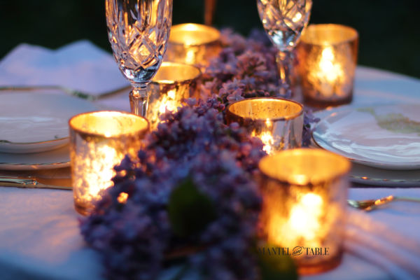Candles and lilacs on an outdoor dinner table at night.