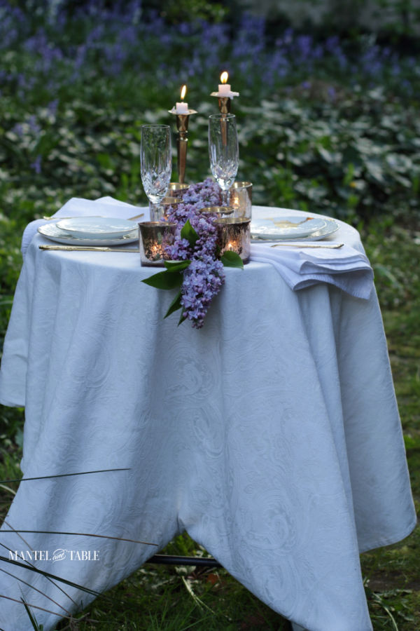 long white tablecloth on an outdoor dinner table for two with candles, lilacs