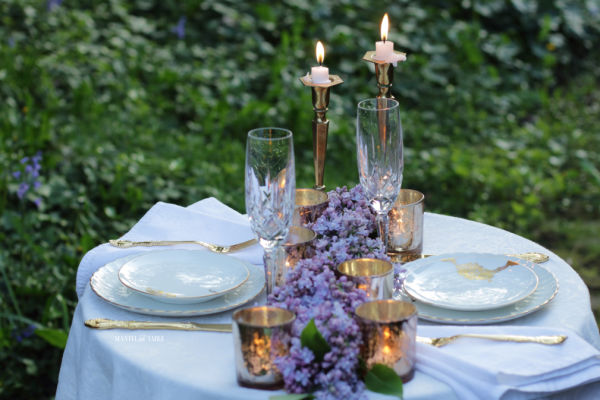 lilac garland on white linen decorates an outdoor candlelight dinner for two