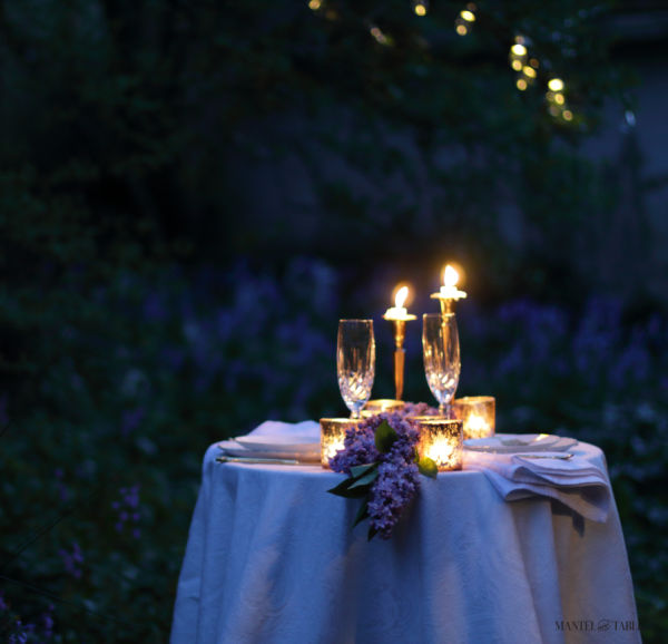 Beautiful table for two outside at night with glowing candles and lights in the trees.