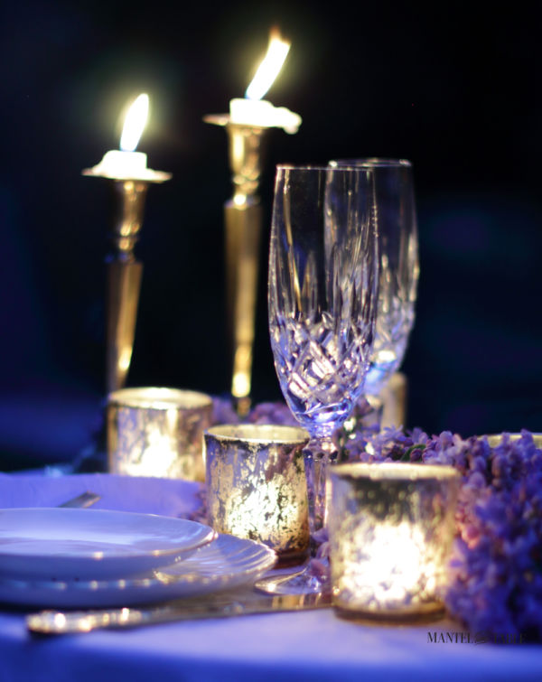 Crystal champagne flutes and candles on an outdoor dinner table at night.