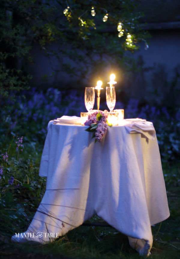 Outdoor candlelight dinner table under the trees with white tablecloth
