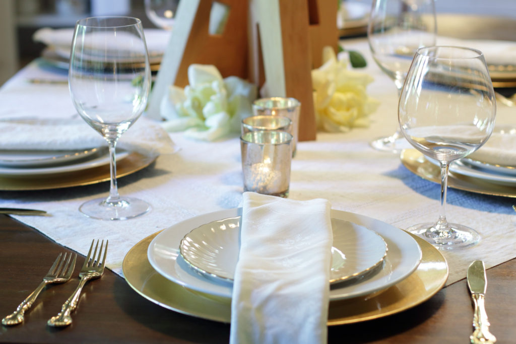 Gold & White place setting with wooden art block & yellow rose centerpiece in the background