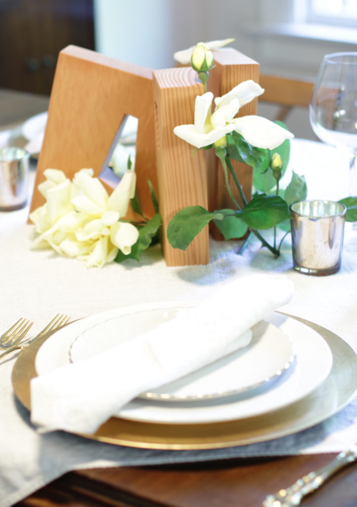 White & gold placesetting, wood art blocks centerpiece with yellow roses. Candles