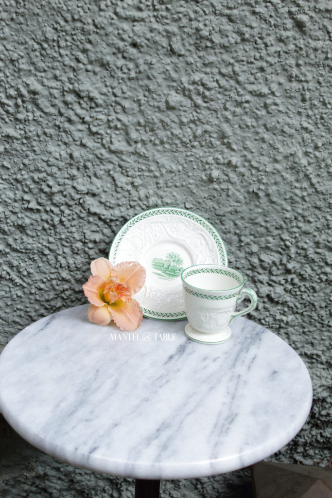 Wedgwood Torbay teacup on marble table against a lot of sage colored textured wall. also a peach daylily.