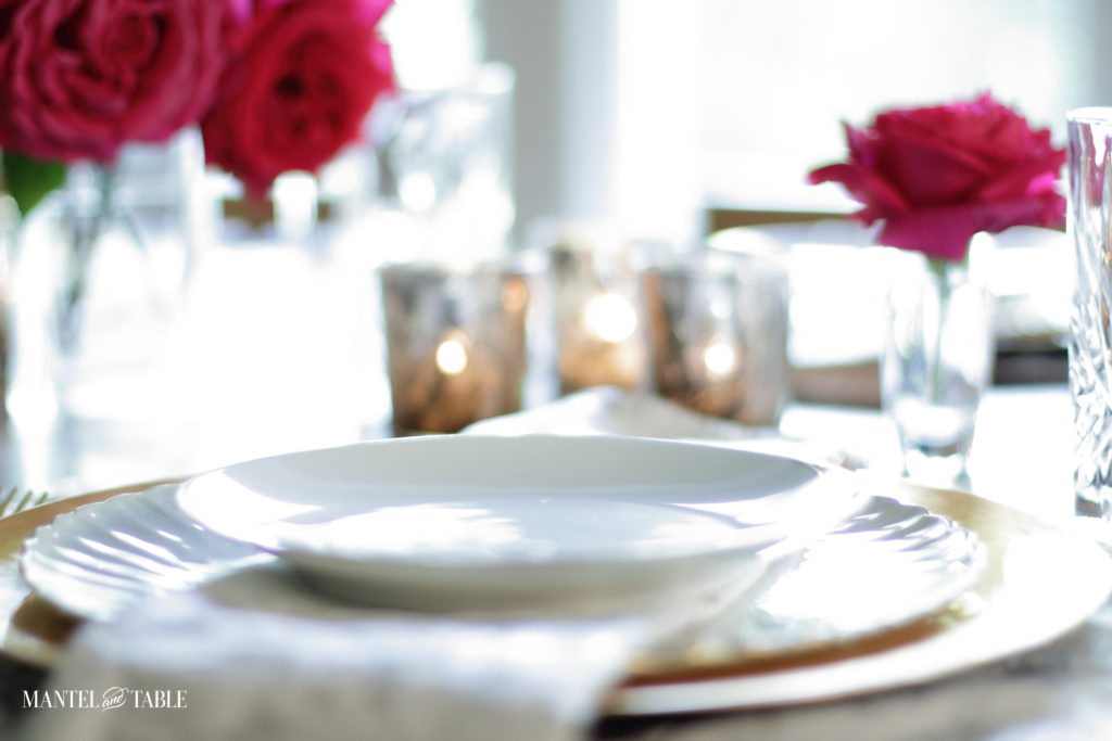 Twinkling gold votive candles looking over a place setting. Deep pink roses