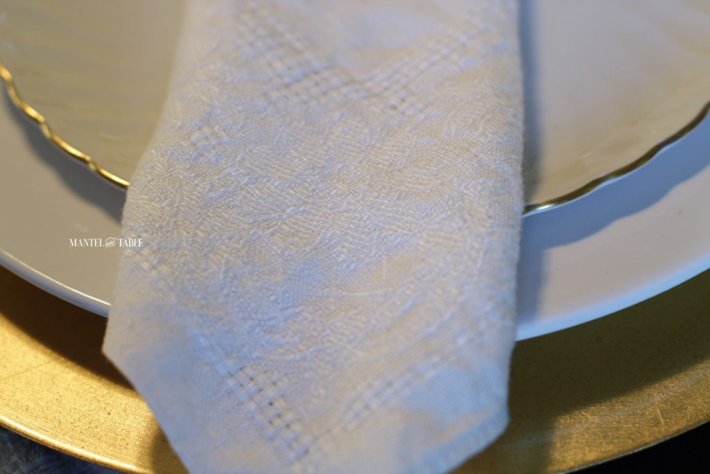Very closeup of textured white napkin on white & gold plate stack