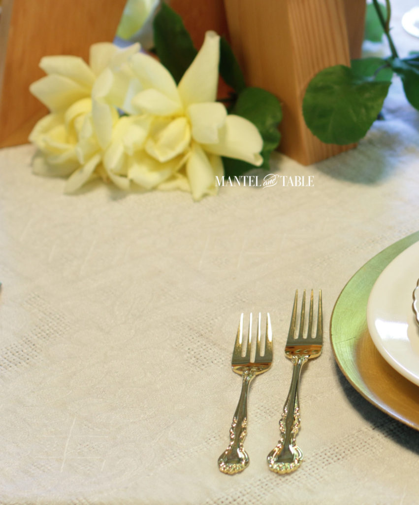 Gold tableware on white tablecloth with yellow roses and golden wood art blocks centerpiece