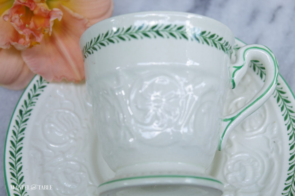 Demitasse cup lying on its side on matching saucer, next to peach daylily