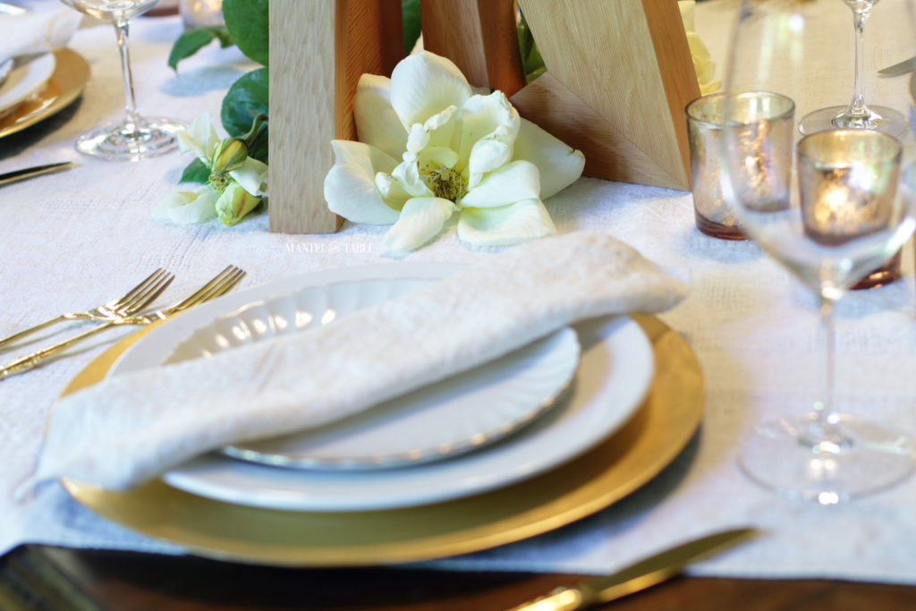 White & gold place setting with yellow rose, work of art centerpiece, and wine glass