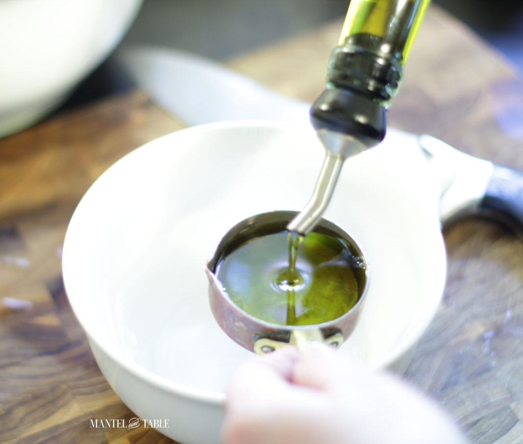 Pouring olive oil into copper measuring cup over white bowl