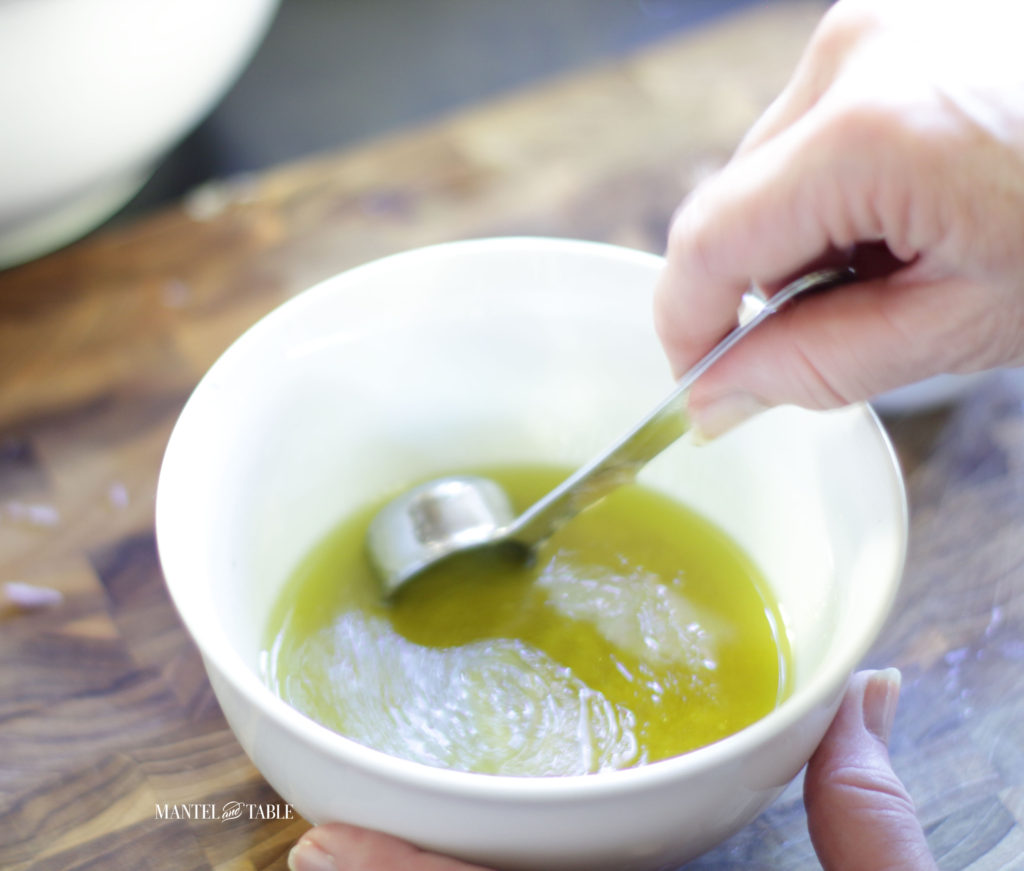 Mixing the grapefruit avocado salad dressing with silver measuring spoon in white bowl