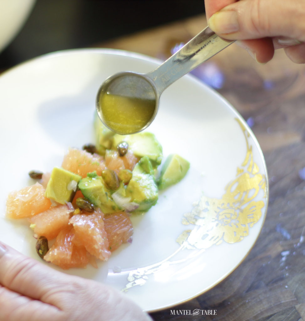 Drizzling dressing over grapefruit avocado salad on white plate with gold leaf flower design