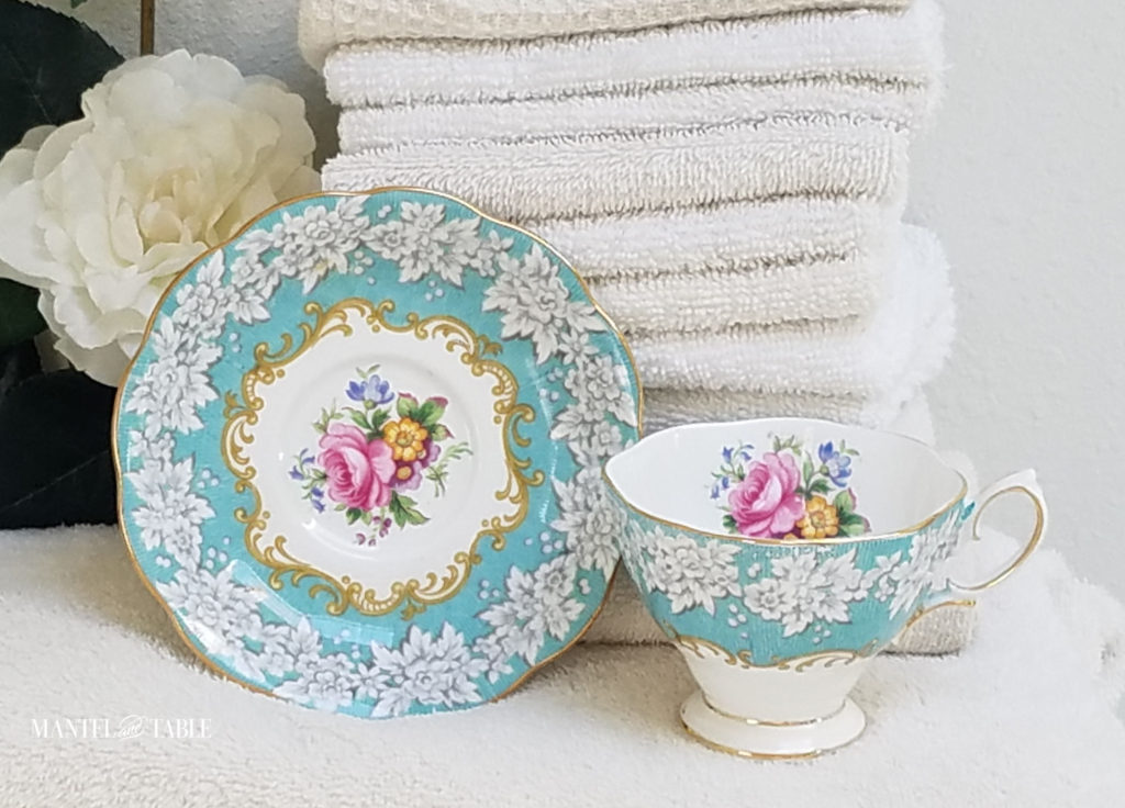 Royal Albert Enchantment Teacup and saucer with a stack of fluffy white towels and a white camellia