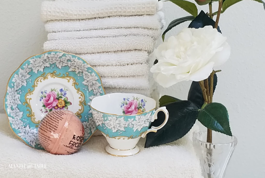 Royal Albert Enchantment Teacup and saucer with a stack of fluffy white towels, pink bath ball