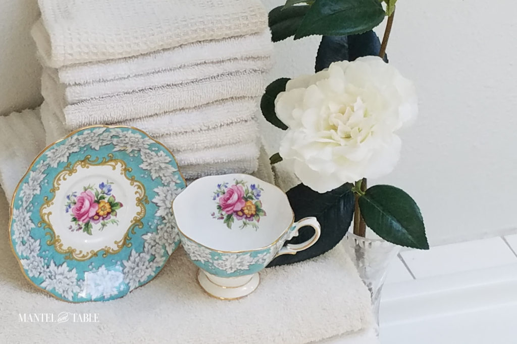 From above, Enchantment Teacup and saucer with a stack of fluffy white towels & camellia branch