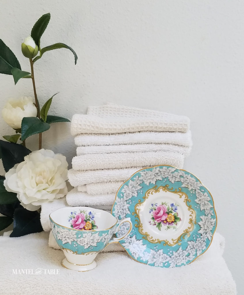 Royal Albert Enchantment Teacup and saucer with a stack of fluffy white towels, white camellia branch