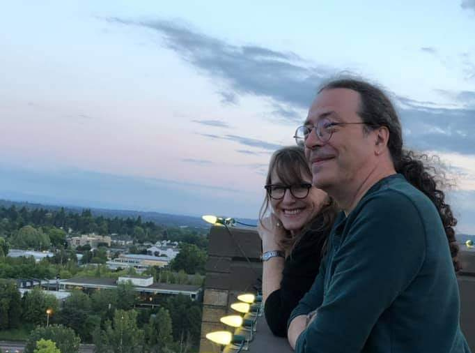 Yours truly and husband with elbows on a balcony overlooking a sunset and city lights