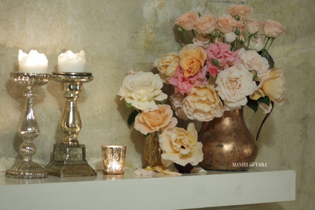Corner of the mantel with garden rose arrangement, tall candles, and votives