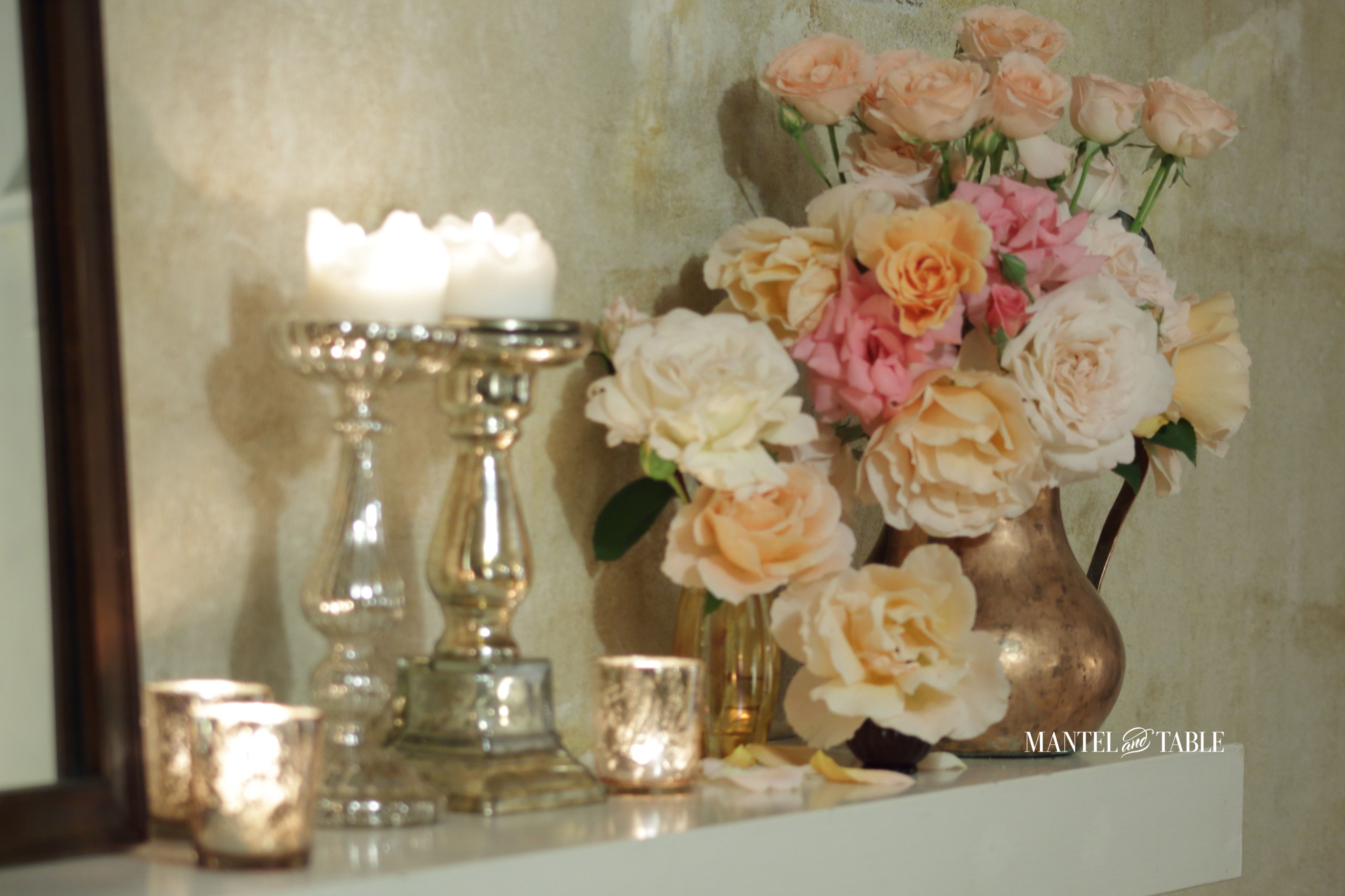 Garden roses in a copper pitcher, and candles on the mantel