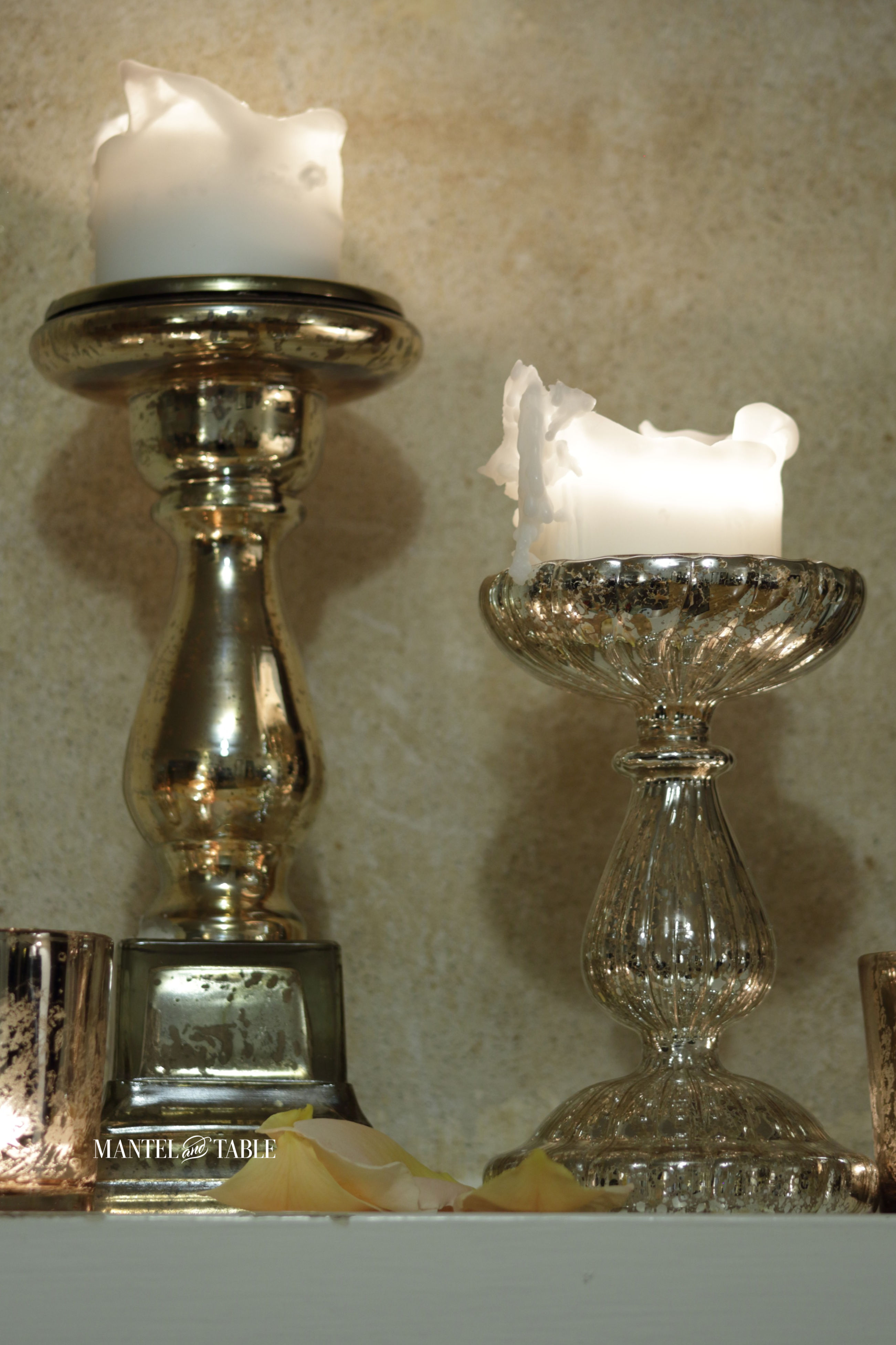 Two gold mercury glass pillar candle sticks with peach rose petals on the mantel