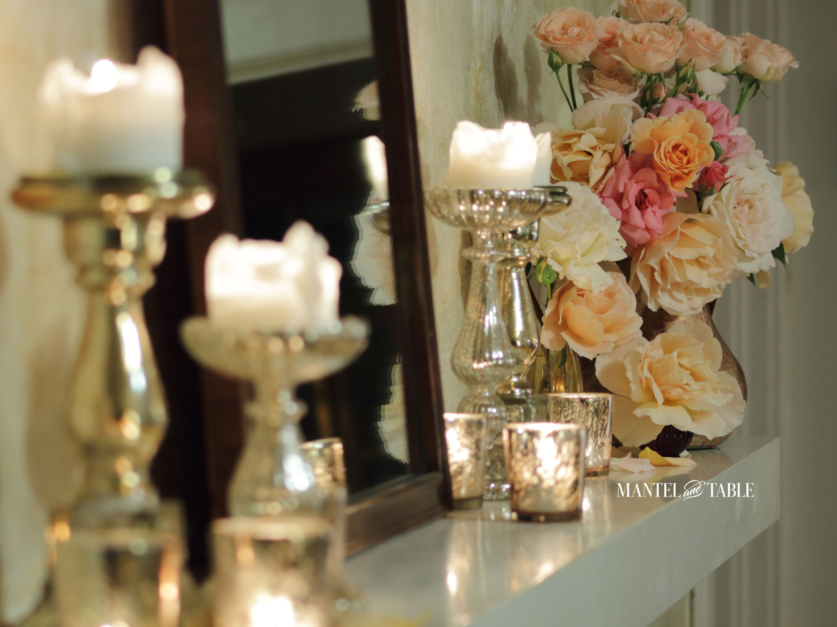 Diagonal shot of garden roses, mirror, and candles on the mantel