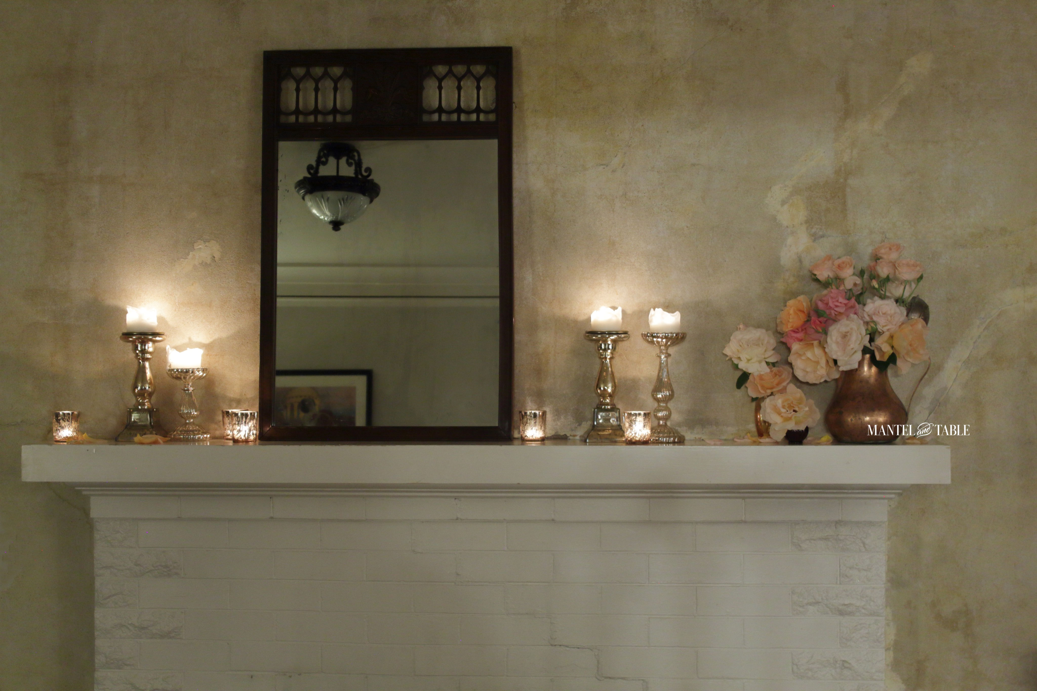 Straight on view of mantel with roses, candles, brown filigree leaning mirror