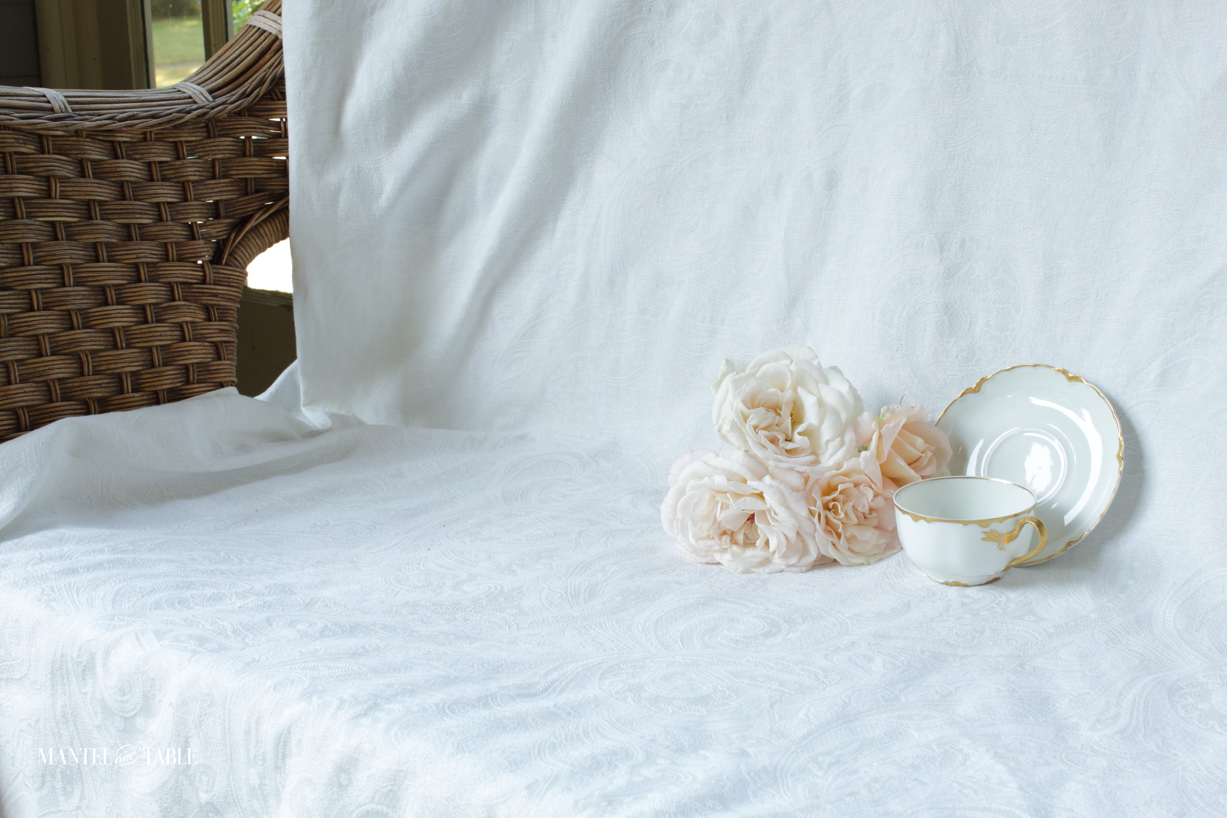 Teacup, saucer, blush roses on white jacquard tablecloth draped over love seat