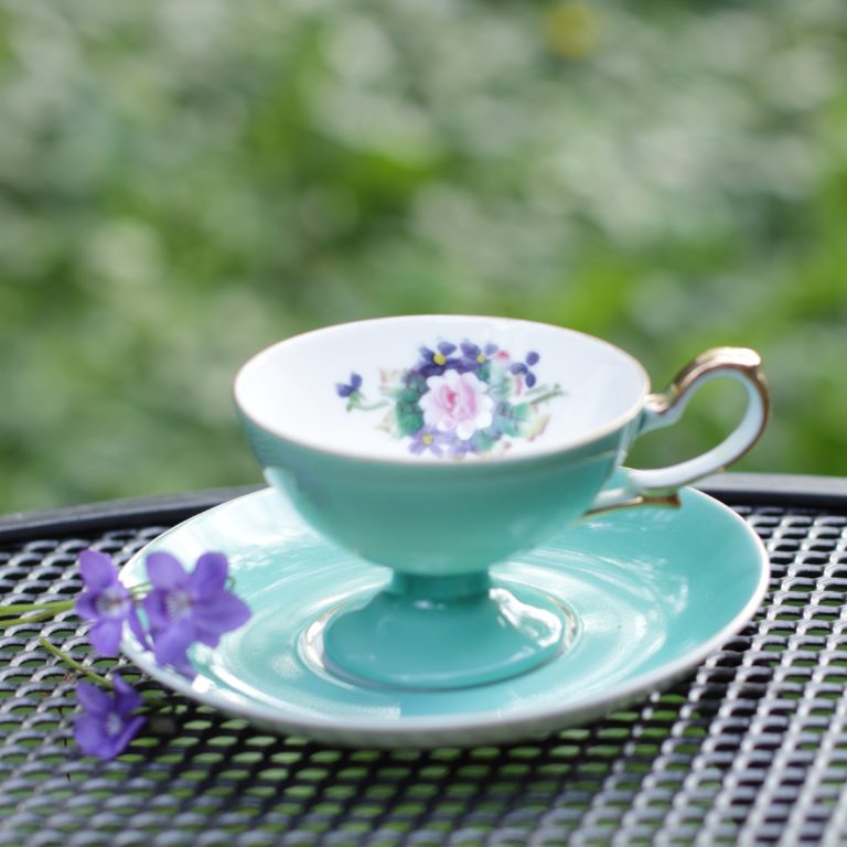 Solid turquoise teacup with white interior and flower. Fresh violets resting on the saucer