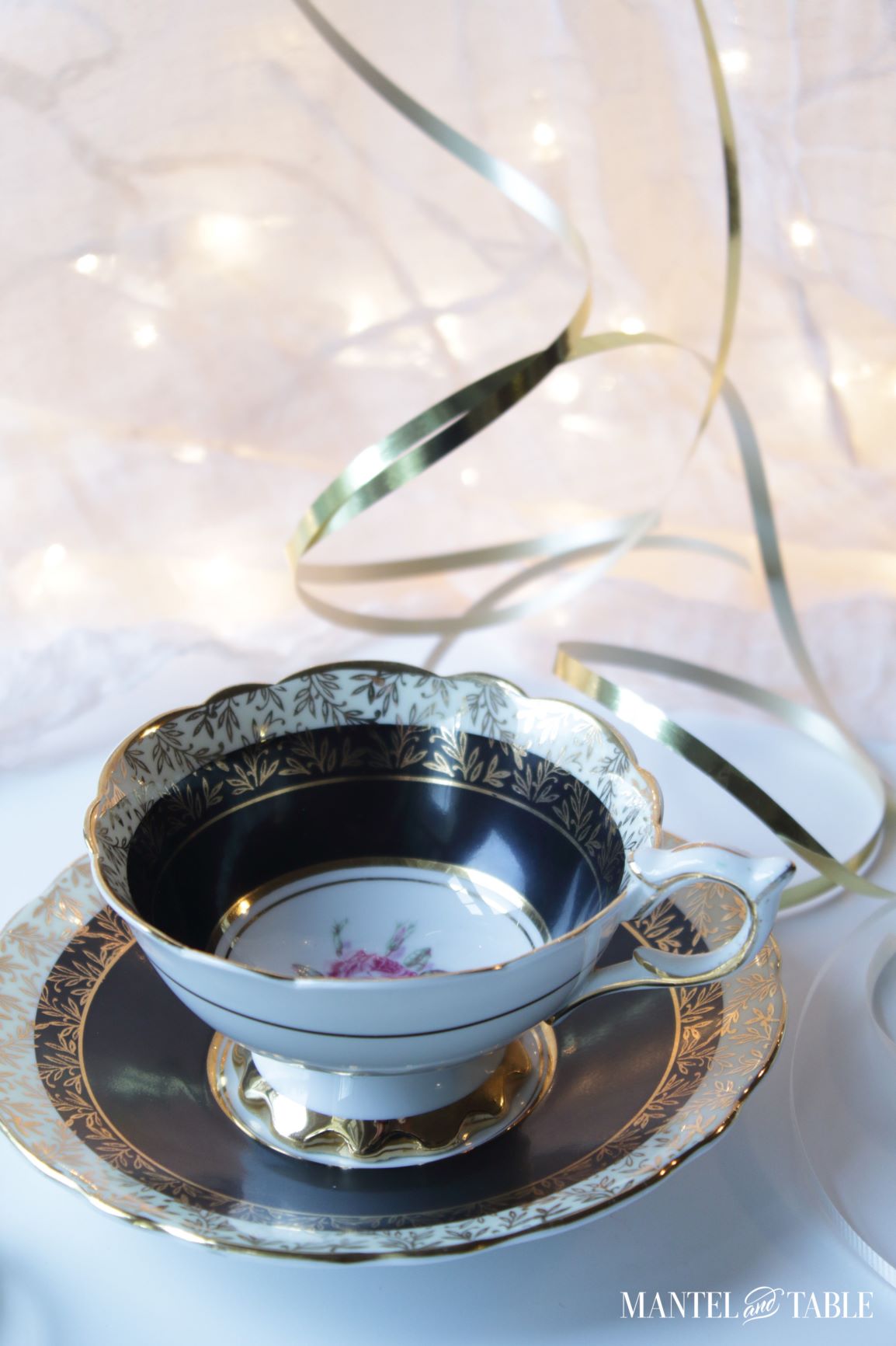 Black and gold teacup with pink flower detail, gold streamers