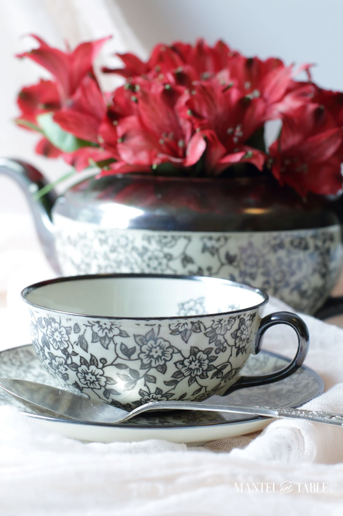 Side view of teacup, silver spoon, and teapot of flowers