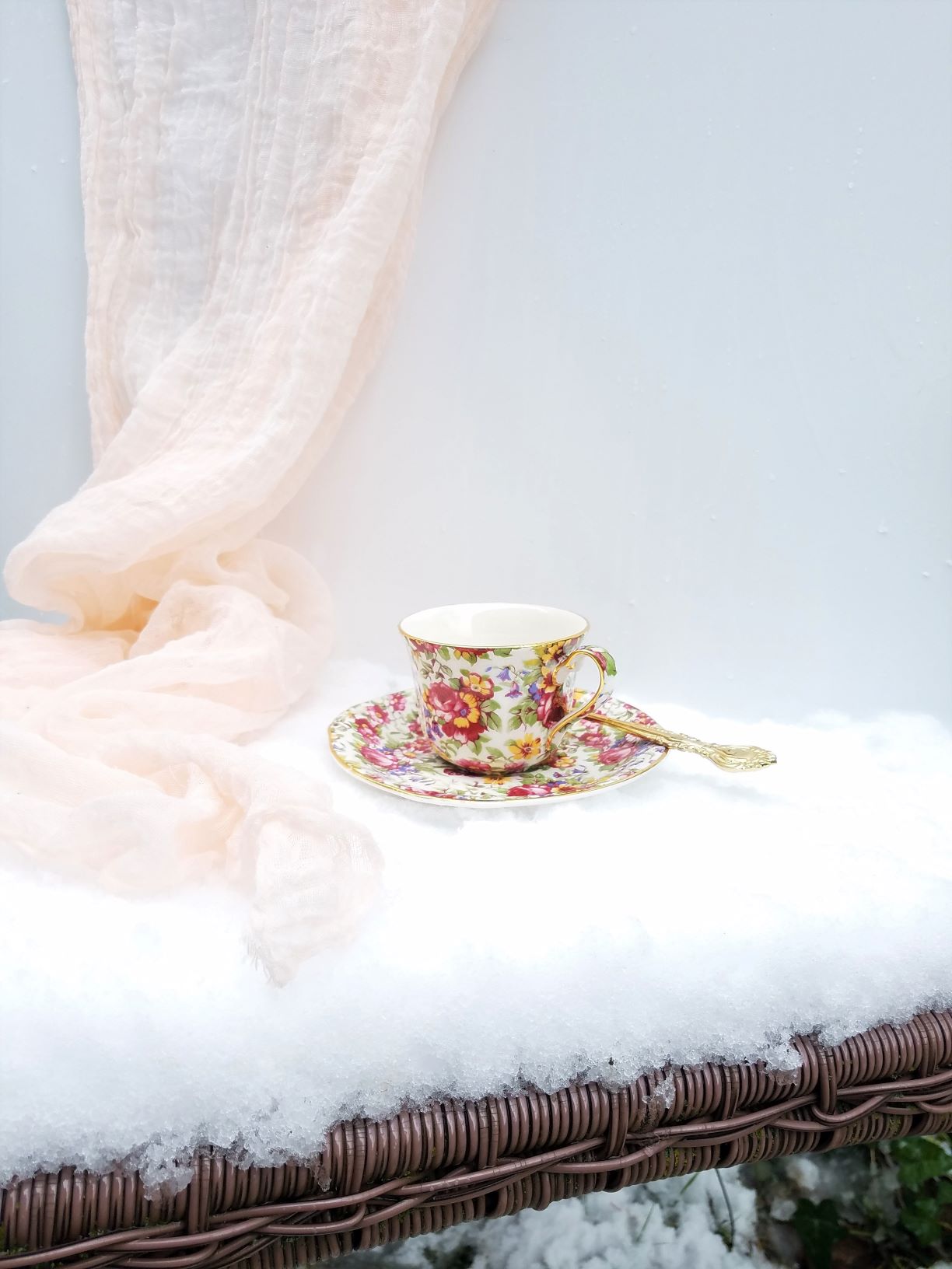 Teacup and saucer on snow covered patio chair with blush voile