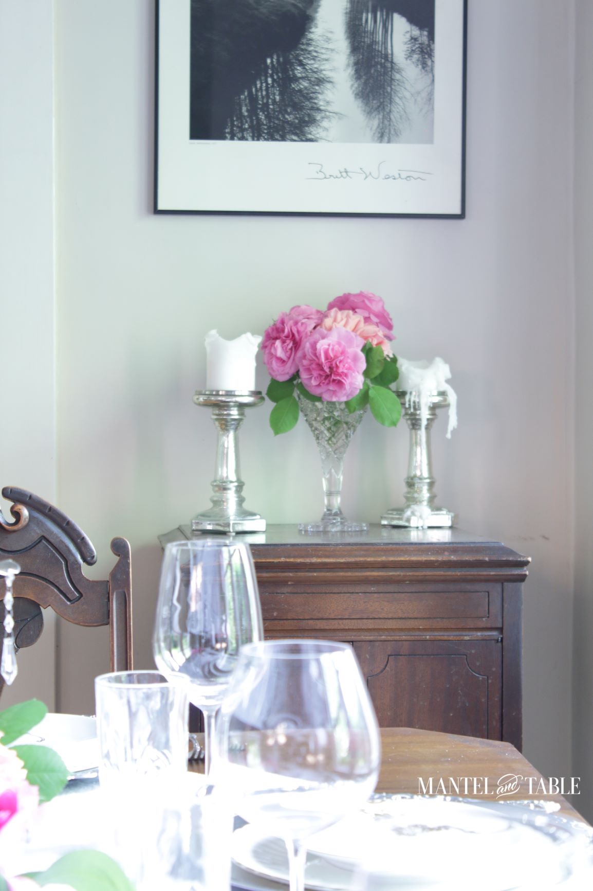 Pink roses in crystal vase between two large candles on cabinet