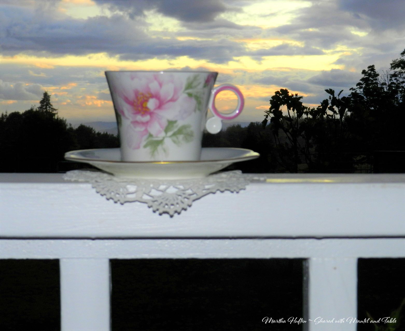 Pink flowered teacup on a railing at sunset