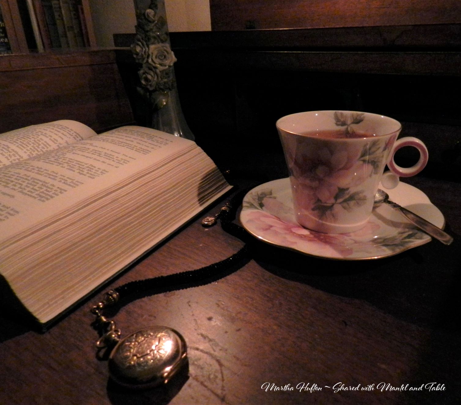Teacup and saucer on a desk with open book and pocket watch