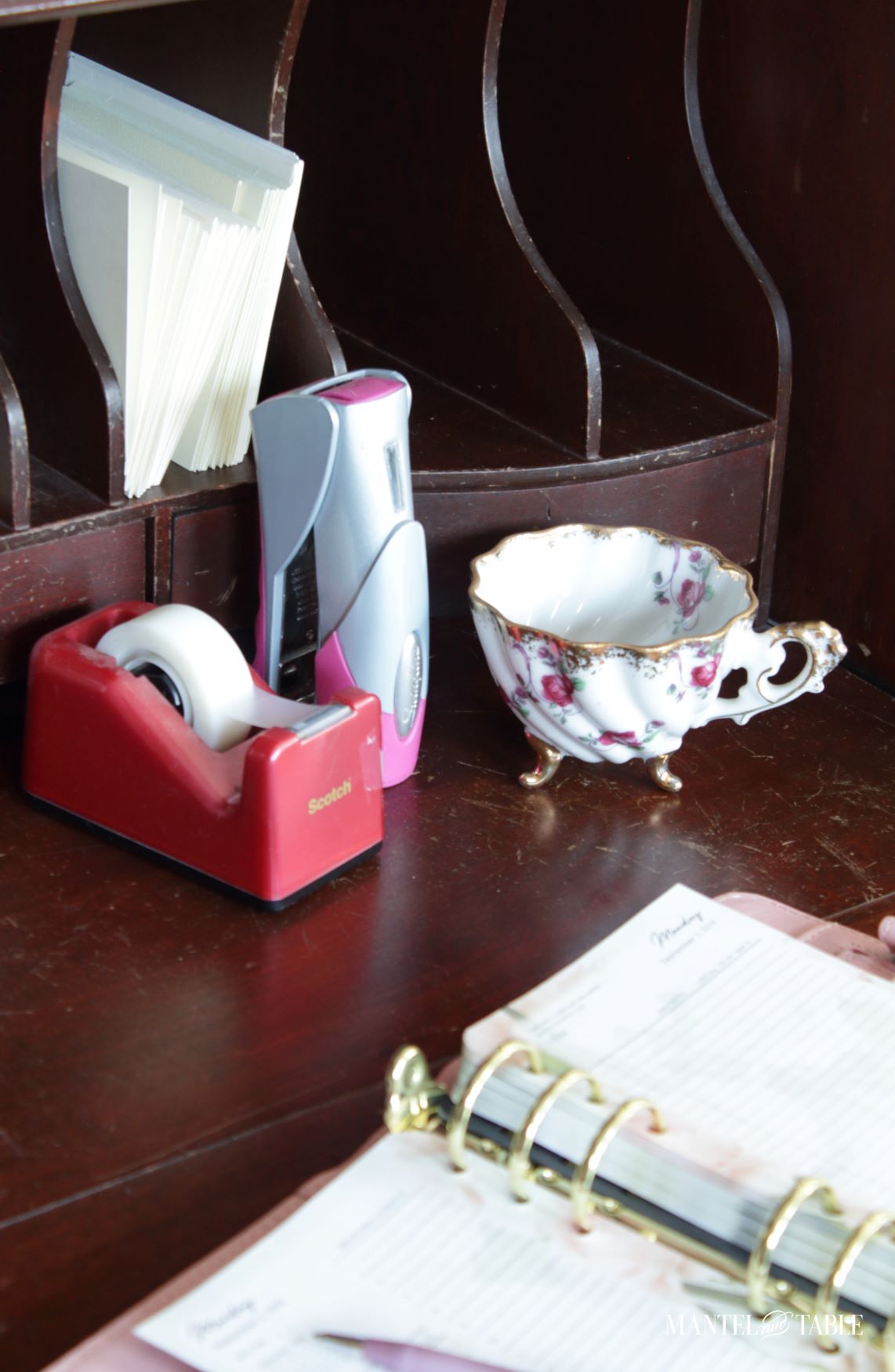 Pink and gold teacup on desk with pink stapler and tape dispenser