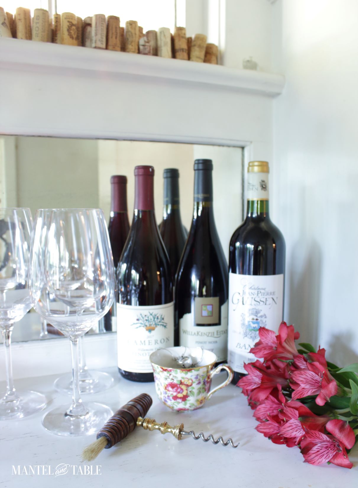 Wine bottles, glasses, corks, flowers, teacup on buffet
