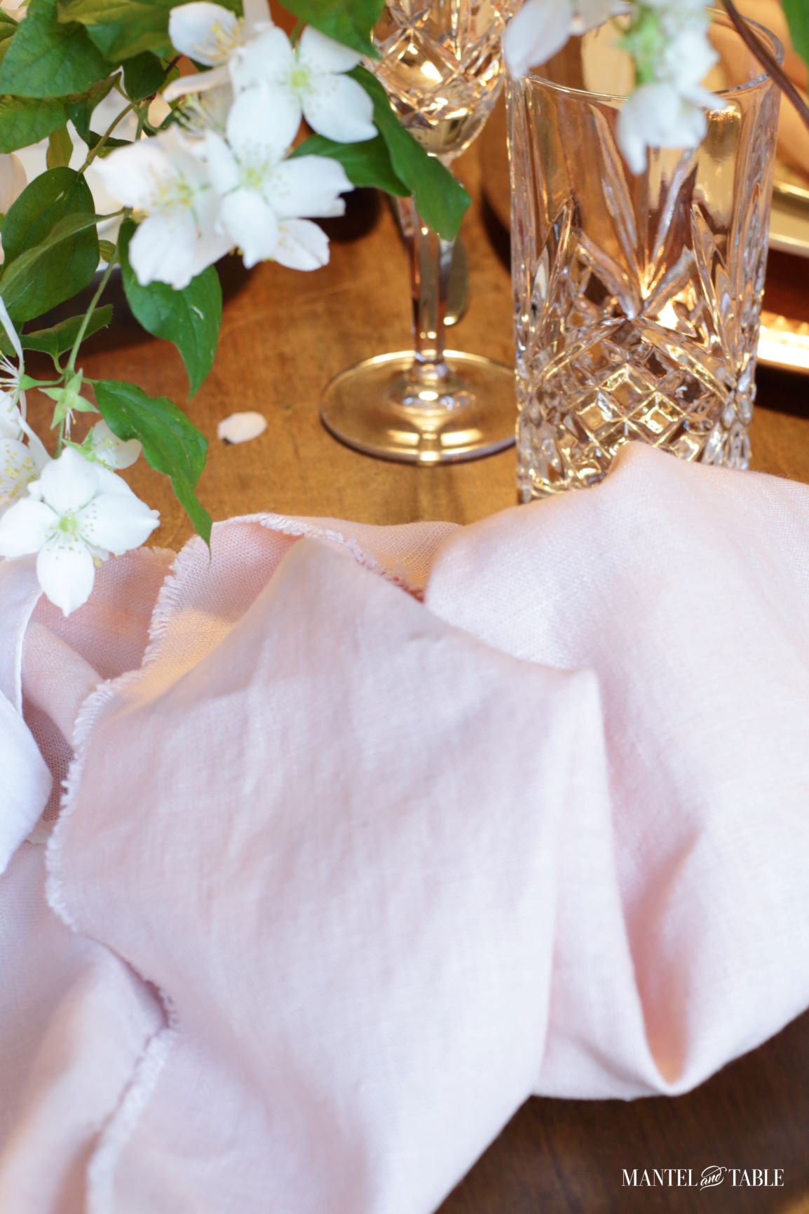 Blush table linens , crystal glasses, and white blossoms