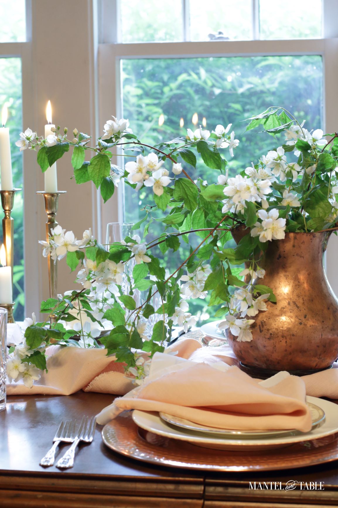 Blush table linens with copper vase of white flowering branches, candles