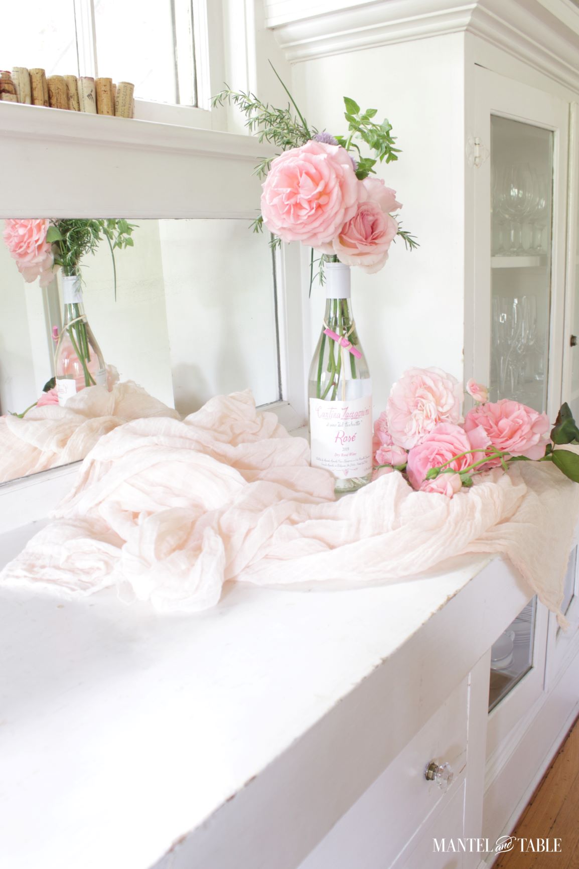 Pink roses in a wine bottle with flowers and fabric on the counter