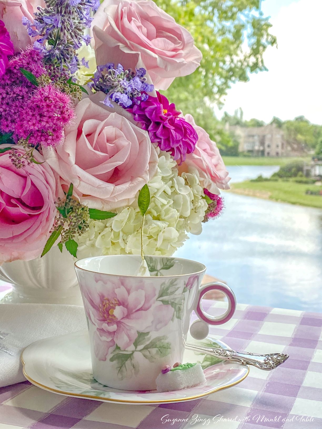 Rose teacup with teabag, pink roses, and view of lake