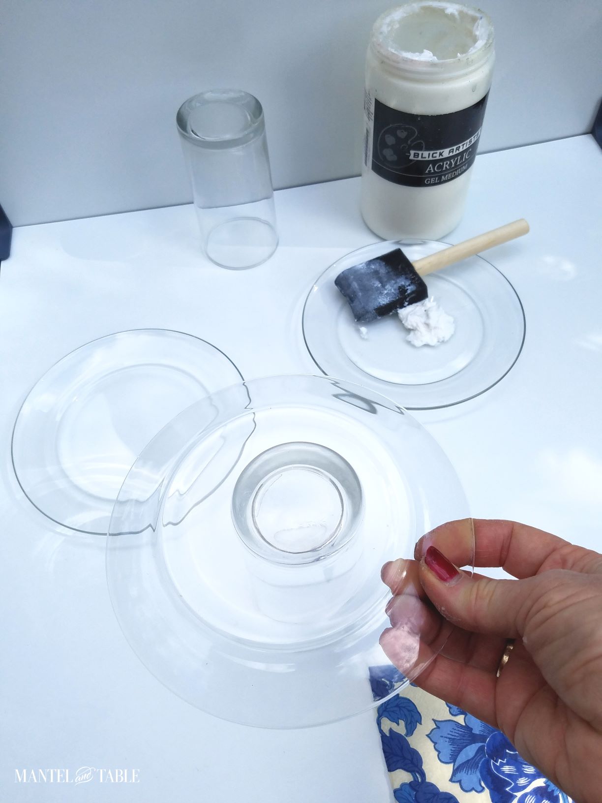 A hand holding a clear salad plate upside down over an upturned water glass
