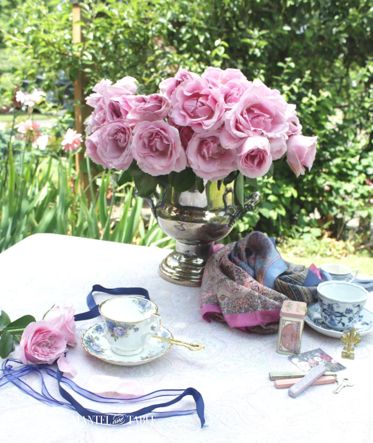 Pink roses in a vase on a table with teacups and other pink and blue props