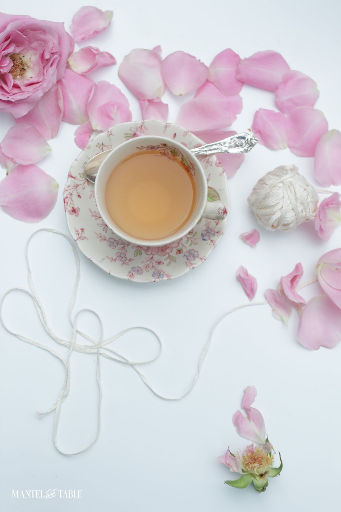 Teacup flat lay on white background with pink rose petals and white yarn
