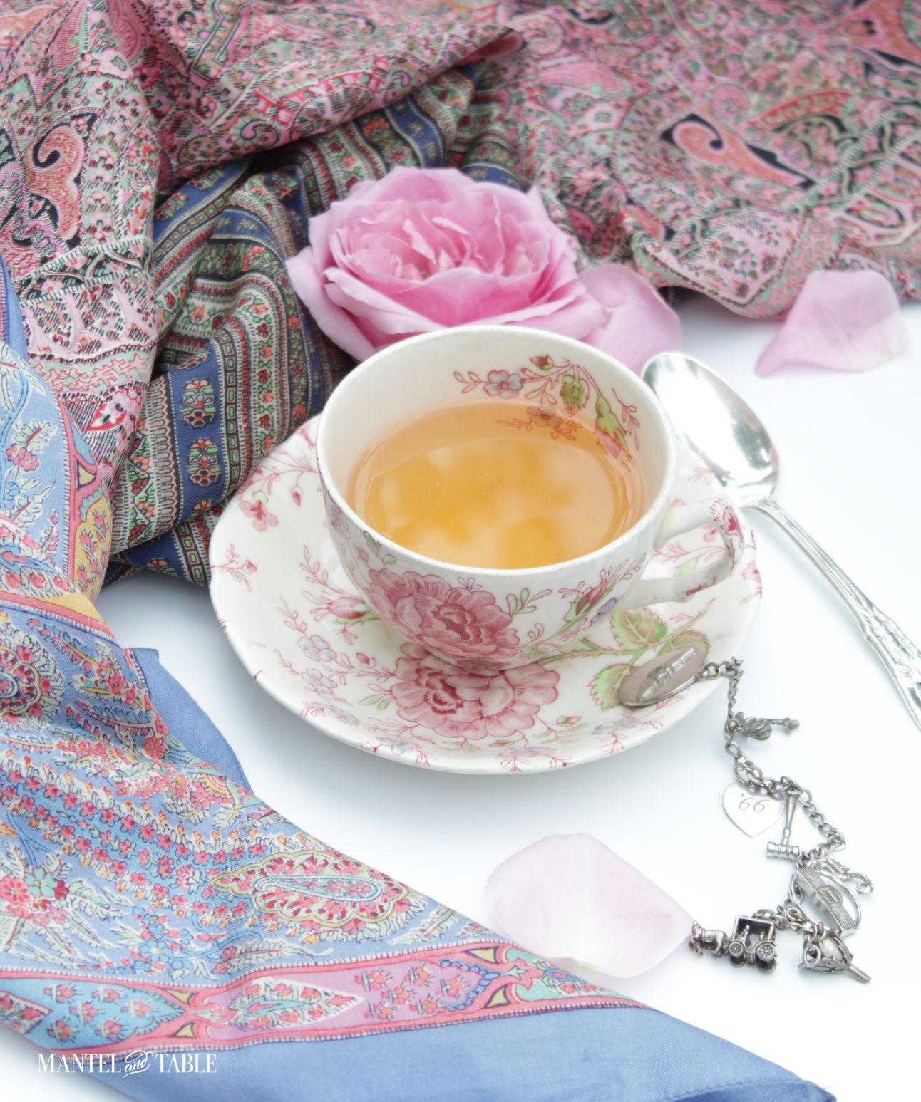 Teacup with silk scarves, a pink rose, and a silver charm bracelet, side view