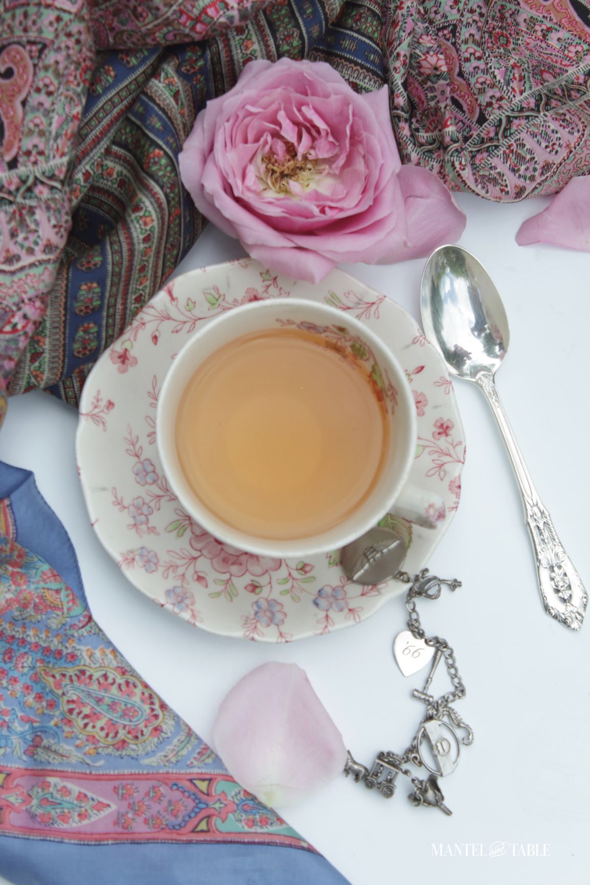 Teacup flat lay with pink and blue silk scarves, a rose, and a silver charm bracelet
