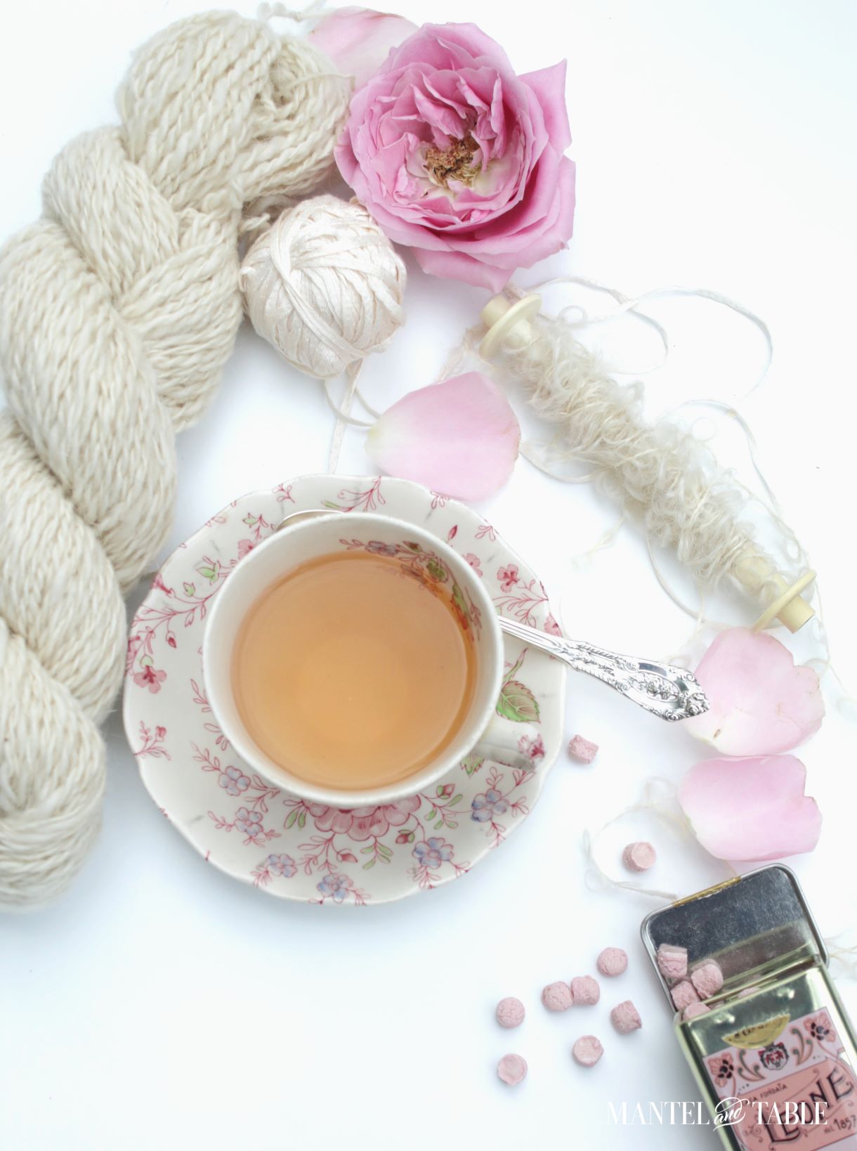 pink flowered teacup flat lay with white yarn, pink rose petals, and tin of pink Leone candies