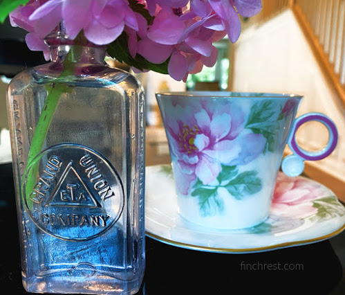 Teacup travels - floral teacup on table with Grand Union bottle