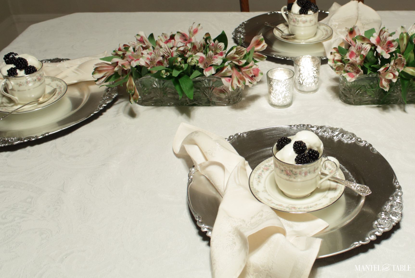 pink flowers, candles, and teacup on silver chargers on table